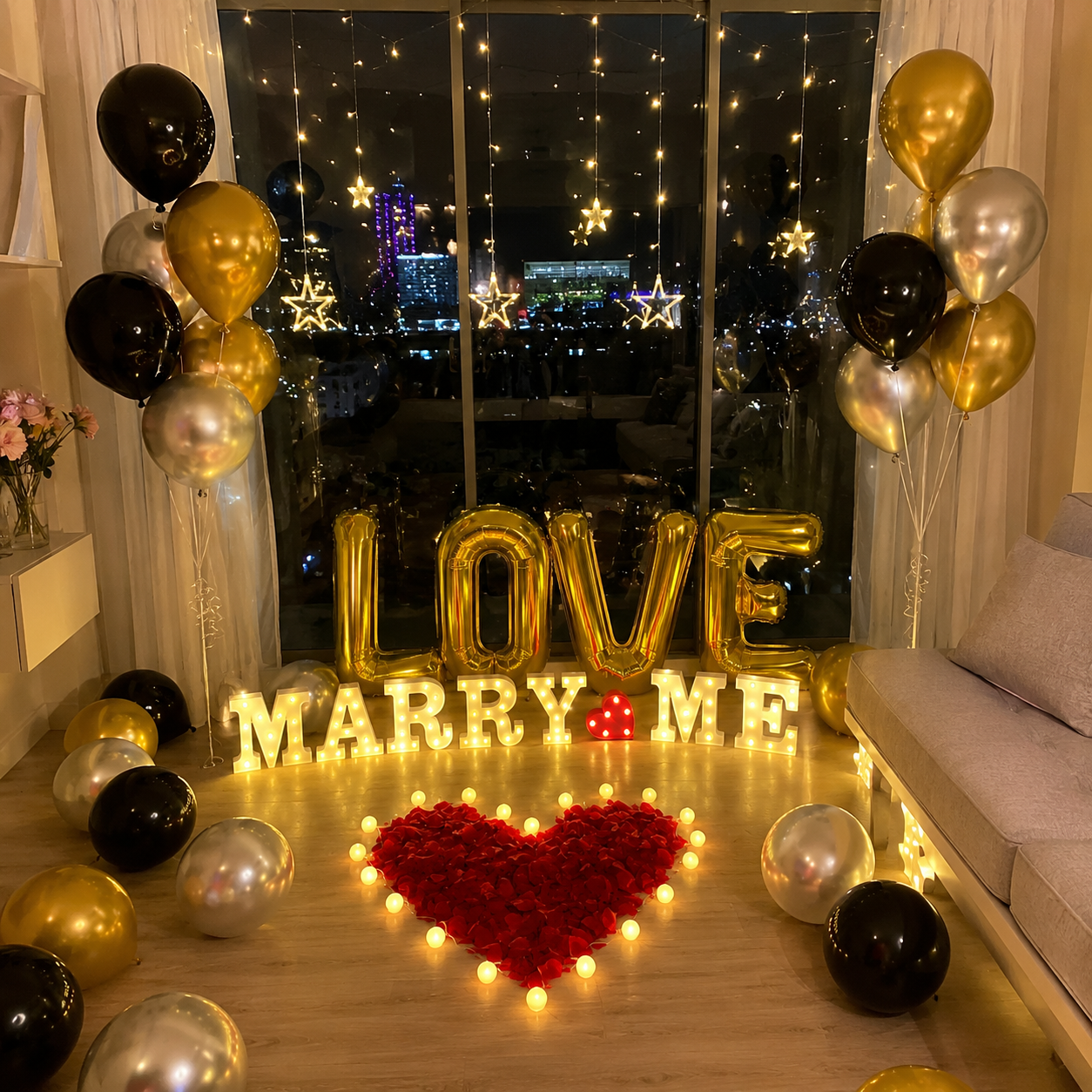 Luxury marriage proposal decoration featuring illuminated LOVE and MARRY ME marquee letters, black gold and silver balloon bouquets, fairy lights and a heart-shaped rose petal arrangement.